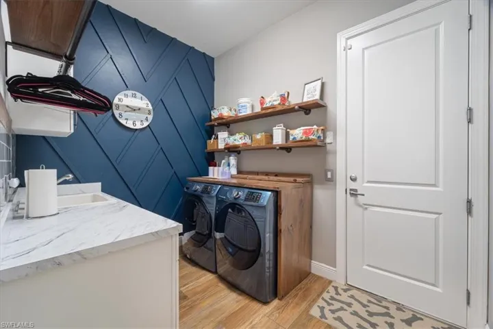 Laundry room featuring baseboards, laundry area, light wood-type flooring, washing machine and dryer, and an accent wall