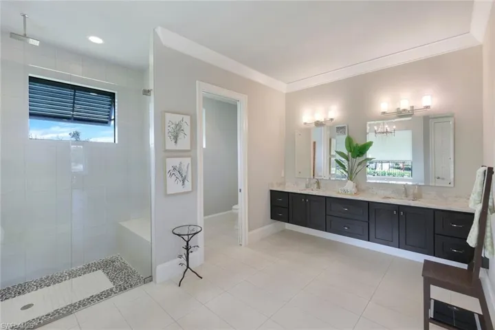 Bathroom with tiled shower, vanity, tile patterned flooring, ornamental molding, and toilet