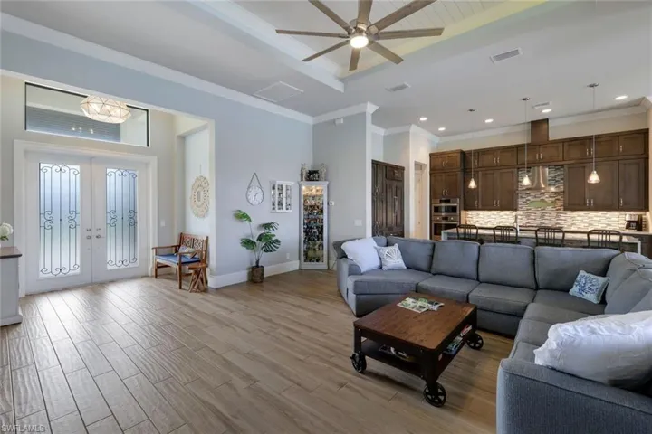 Living room featuring light wood-type flooring, crown molding, a tray ceiling, ceiling fan, and french doors