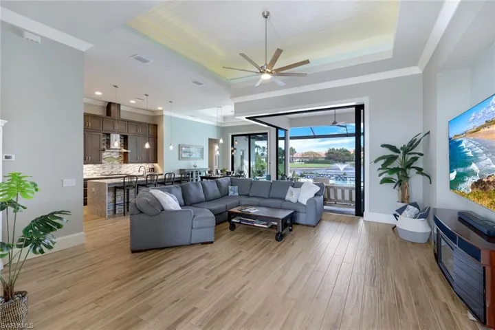 Living room featuring ceiling fan, ornamental molding, a raised ceiling, and light hardwood / wood-style floors