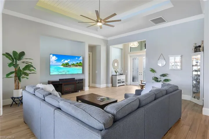 Living room featuring light hardwood / wood-style floors, a raised ceiling, a fireplace, crown molding, and ceiling fan