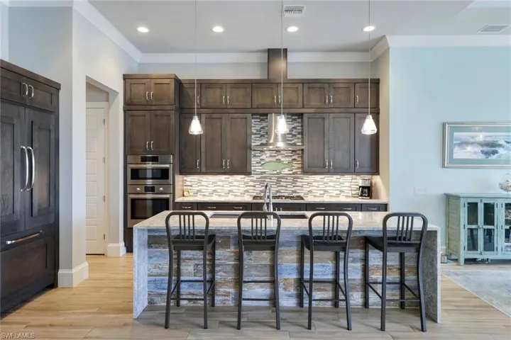Kitchen featuring appliances with stainless steel finishes, decorative backsplash, a breakfast bar area, a center island with sink, and wall chimney range hood