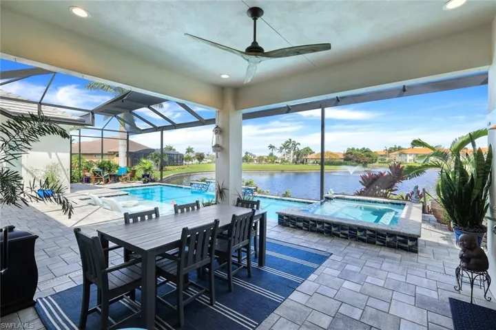 View of patio featuring a water view, glass enclosure, ceiling fan, and a swimming pool with hot tub