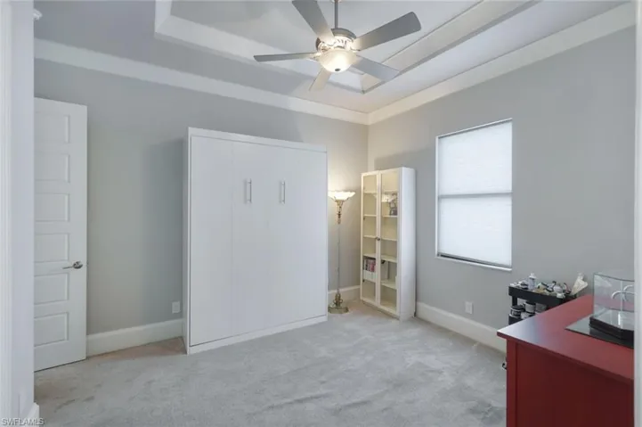 Unfurnished office with ceiling fan, light colored carpet, and a raised ceiling