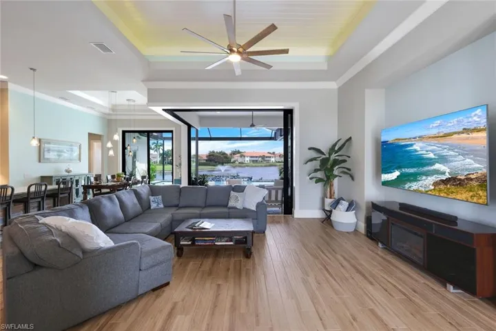 Living room featuring ceiling fan, ornamental molding, a raised ceiling, and light hardwood / wood-style floors