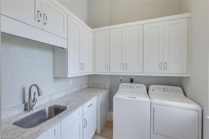 Laundry room featuring light wood-type flooring, sink, washing machine and clothes dryer, and cabinets