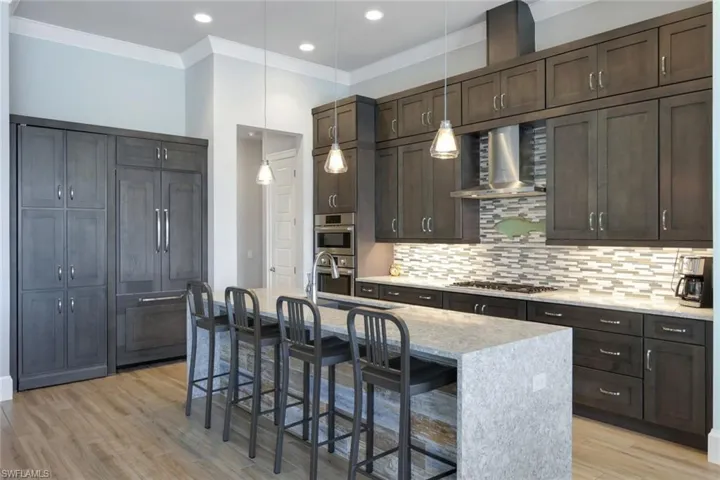 Kitchen with a breakfast bar, light hardwood / wood-style floors, appliances with stainless steel finishes, and wall chimney range hood