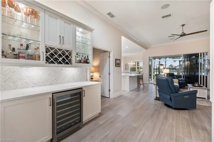 Bar with beverage cooler, white cabinetry, decorative backsplash, ornamental molding, and light wood-type flooring