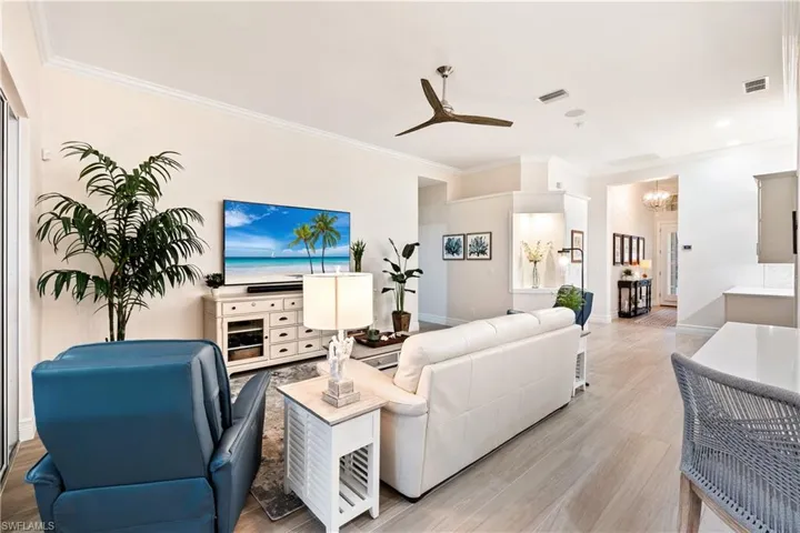 Living room featuring ceiling fan with notable chandelier, ornamental molding, and light wood-type flooring