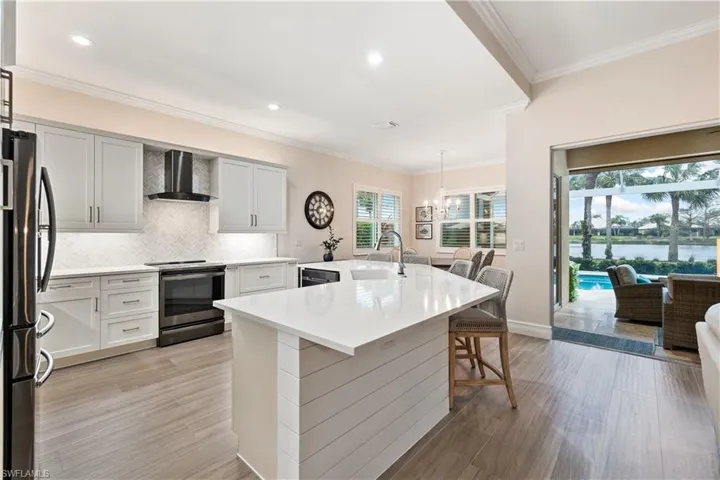 Kitchen featuring hanging light fixtures, a kitchen island with sink, a breakfast bar, stainless steel appliances, and wall chimney exhaust hood