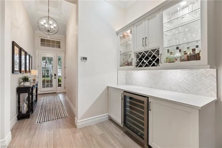 Bar with crown molding, light wood-type flooring, an inviting chandelier, backsplash, and beverage cooler