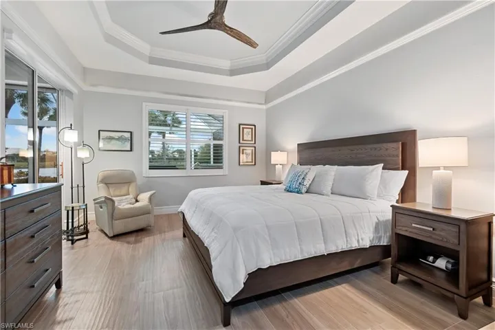Bedroom with ceiling fan, a raised ceiling, ornamental molding, and light hardwood / wood-style floors