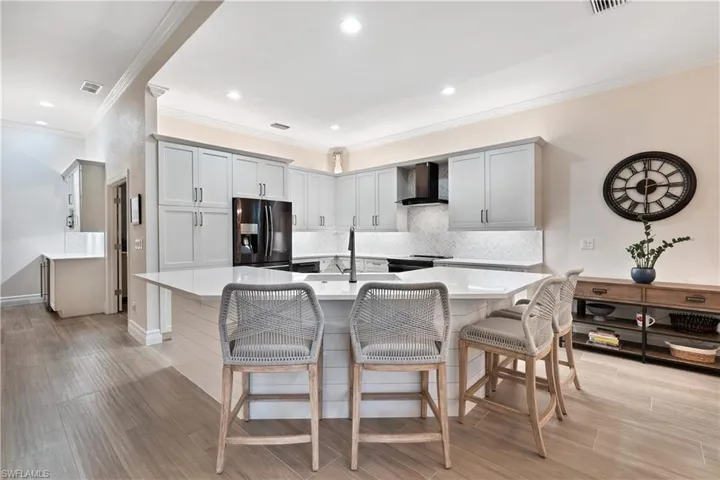 Kitchen featuring a breakfast bar area, fridge with ice dispenser, a center island with sink, and wall chimney exhaust hood
