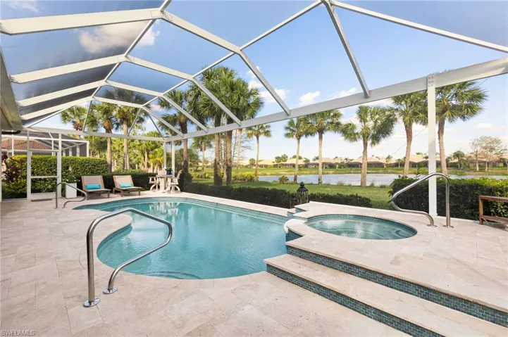 View of swimming pool featuring a pool with connected hot tub, glass enclosure, a patio area, and a water view