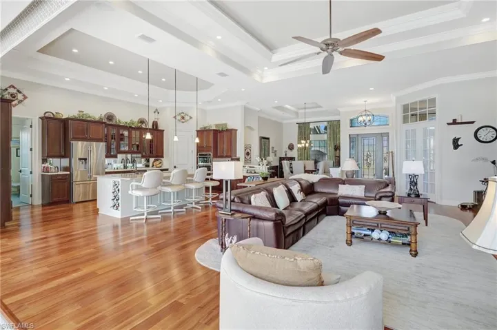 Living area featuring a tray ceiling, crown molding, light wood-type flooring, visible vents, and ceiling fan