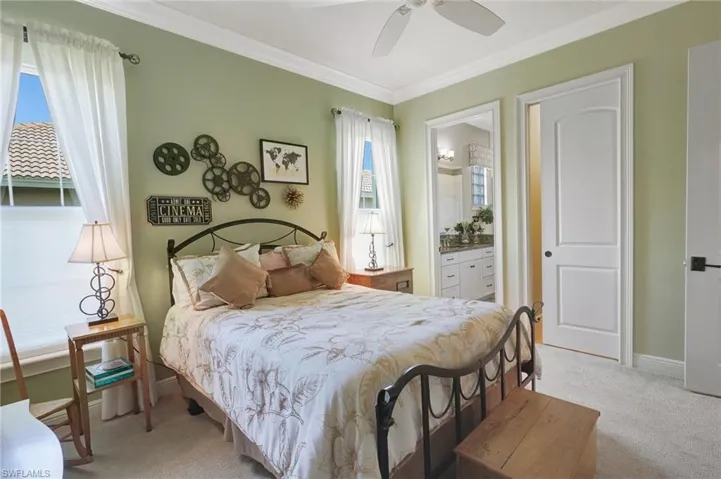 Bedroom with baseboards, ornamental molding, ceiling fan, ensuite bath, and light colored carpet
