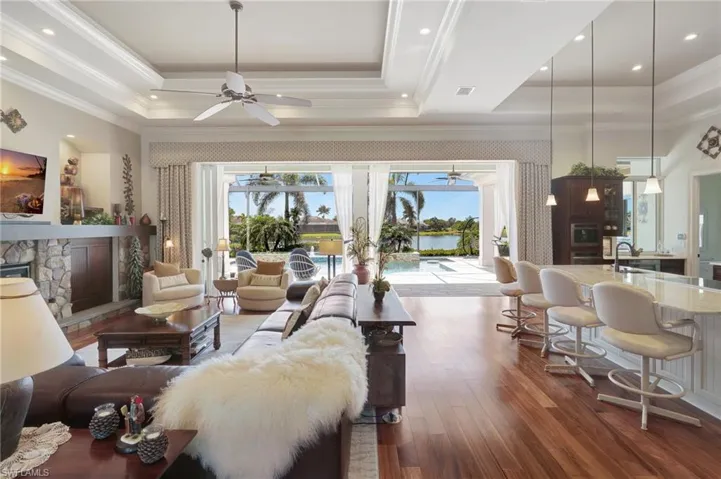 Living room with a ceiling fan, a tray ceiling, crown molding, and wood finished floors