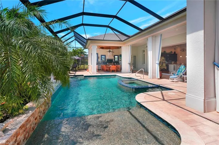 View of swimming pool featuring a lanai, a pool with connected hot tub, palm trees, and a  large covered lanai with protection and outdoor fully equipped kitchen