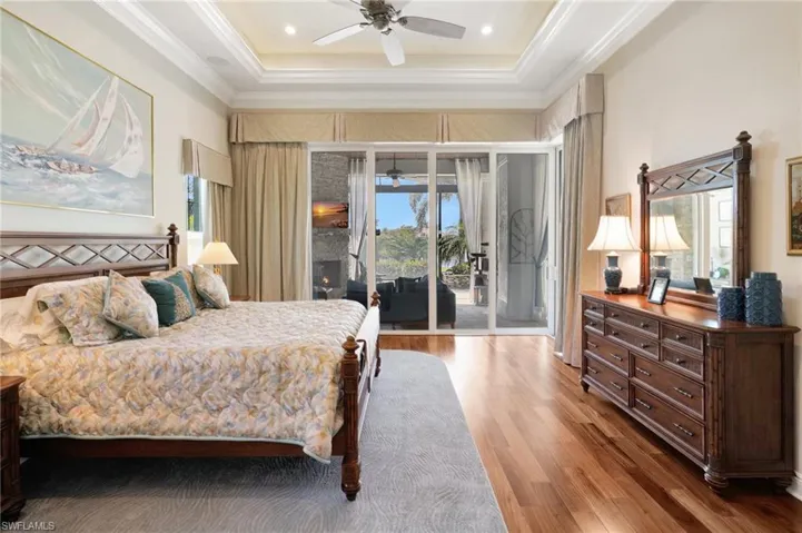 Bedroom featuring access to exterior, wood finished floors, crown molding, and a raised ceiling
