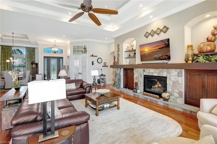 Living room featuring a stone fireplace, a ceiling fan, wood finished floors, and a raised ceiling