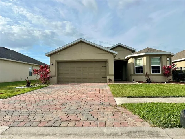 Ranch-style home featuring a front yard, stucco siding, decorative driveway, and an attached garage
