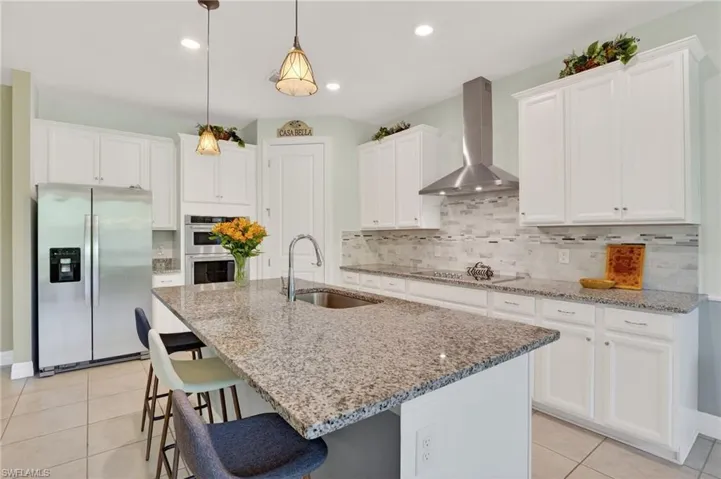 This bright and airy kitchen features a built-in oven, beautiful white cabinetry, a convenient center island with a sink, and tile flooring.