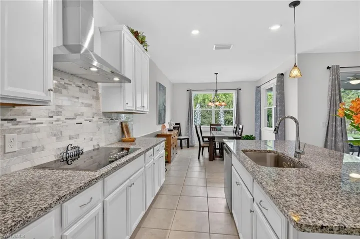 This bright and airy kitchen features beautiful t stone countertops, elegant white cabinetry, a convenient center island with sink, and tile flooring.