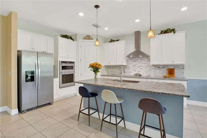 This bright and airy kitchen features a built-in oven, beautiful white cabinetry, a convenient center island with a sink, and tile flooring.