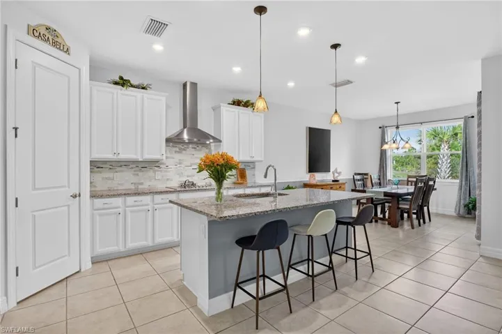 This bright and airy kitchen features a built-in oven, beautiful white cabinetry, a convenient center island with a sink, and tile flooring.