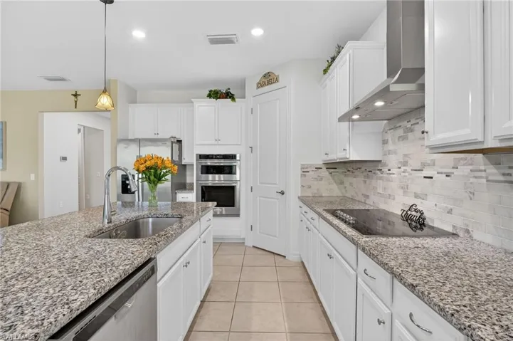 This bright and airy kitchen features a built-in oven, beautiful white cabinetry, a convenient center island with a sink, and tile flooring.