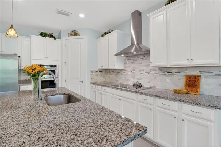 This bright and airy kitchen features a built-in oven, beautiful white cabinetry, a convenient center island with a sink, and tile flooring.