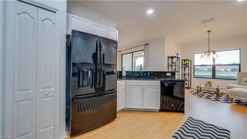 Kitchen with black appliances, hanging lights, white cabinetry, light wood-type flooring, and a peninsula