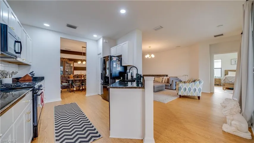 Kitchen featuring dark stone countertops, black appliances, hanging lights, white cabinetry, and light wood-type flooring