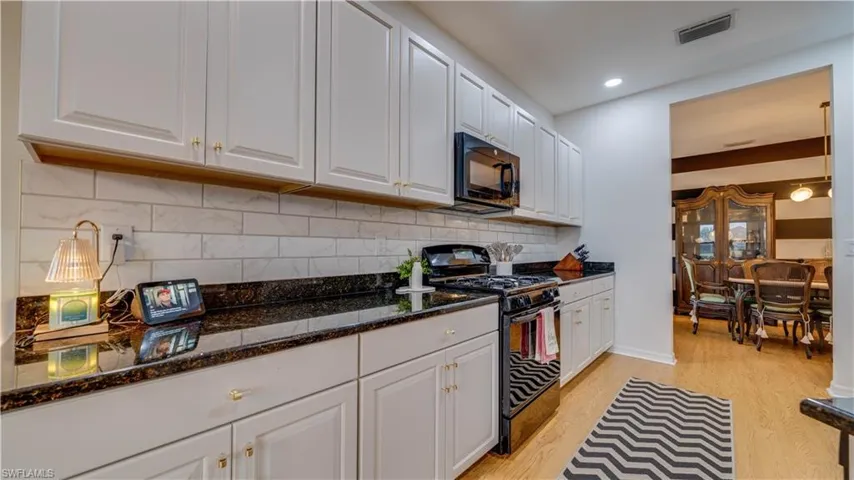 Kitchen with black appliances, white cabinets, dark stone counters, light wood finished floors, and recessed lighting