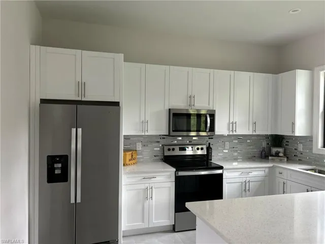 Kitchen with appliances with stainless steel finishes, light stone countertops, white cabinets, and backsplash