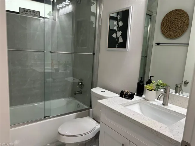 Full bathroom with combined bath / shower with glass door, toilet, and vanity