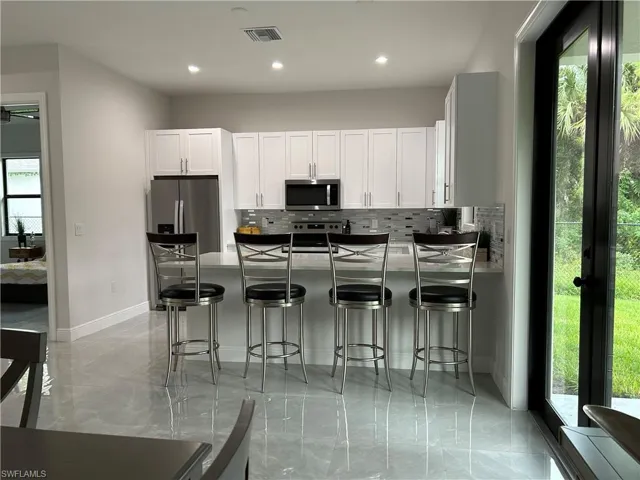 Kitchen with white cabinets, stainless steel appliances, backsplash, and a healthy amount of sunlight