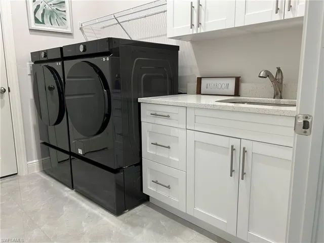 Laundry room with separate washer and dryer, light tile patterned floors, sink, and cabinets