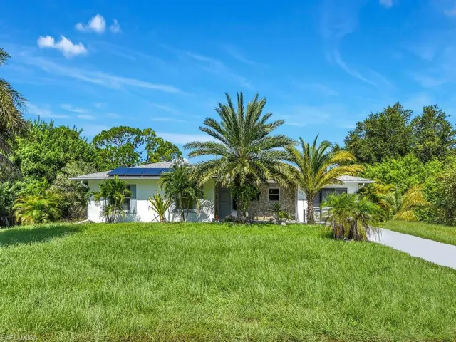 View of front of home with solar panels, stucco siding, and a front lawn
