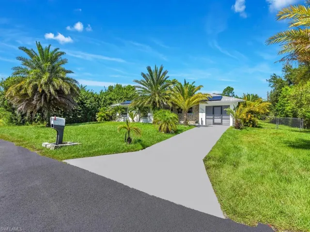 View of property hidden behind natural elements featuring fence, a front lawn, roof mounted solar panels, and concrete driveway