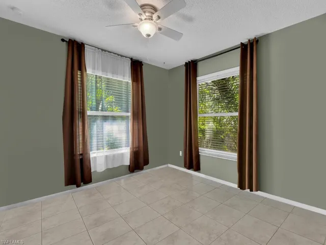 Empty room featuring light tile patterned flooring, baseboards, ceiling fan, and a textured ceiling