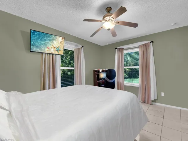 Bedroom featuring light tile patterned flooring, a textured ceiling, baseboards, and ceiling fan