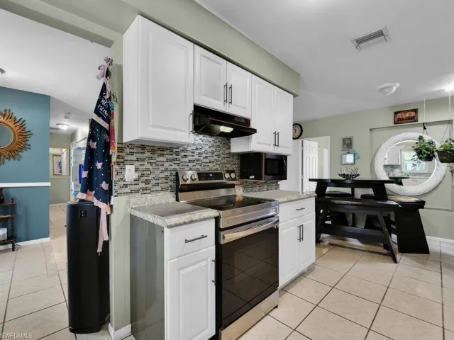 Kitchen with light tile patterned flooring, tasteful backsplash, under cabinet range hood, electric stove, and visible vents