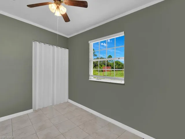 Empty room featuring baseboards, light tile patterned floors, ornamental molding, and a ceiling fan