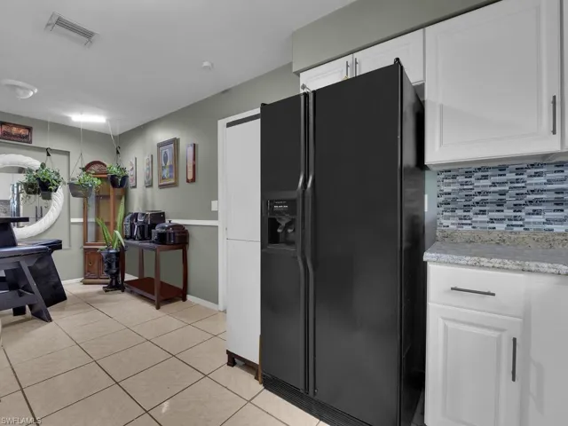 Kitchen featuring white cabinets, visible vents, black refrigerator with ice dispenser, backsplash, and light tile patterned floors