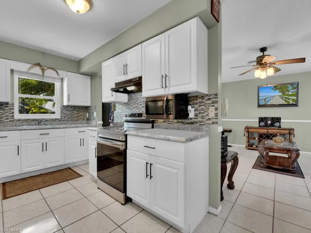 Kitchen featuring backsplash, light tile patterned floors, appliances with stainless steel finishes, and under cabinet range hood