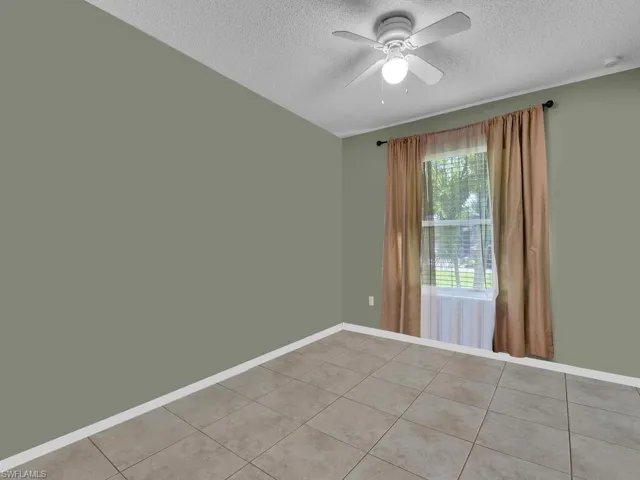 Spare room featuring light tile patterned floors, a textured ceiling, baseboards, and a ceiling fan