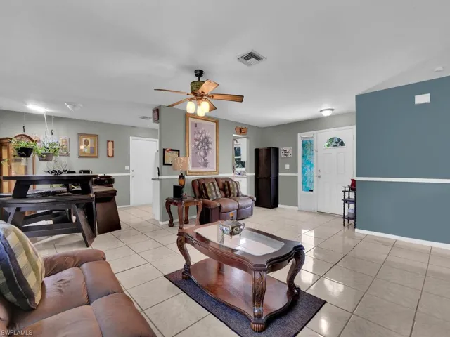 Living area with light tile patterned floors, baseboards, ceiling fan, and visible vents