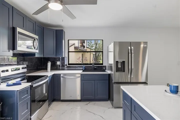 Kitchen featuring appliances with stainless steel finishes, light marble finish flooring, blue cabinetry, tasteful backsplash, and light stone counters