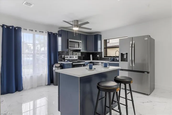 Kitchen featuring appliances with stainless steel finishes, a kitchen bar, light marble finish flooring, and light countertops